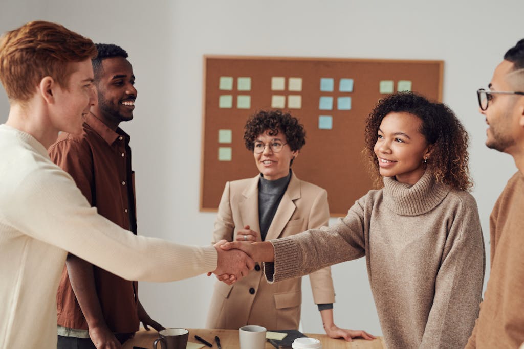 A diverse group of colleagues shaking hands after securing a mergers and acquisitions deal in a productive office meeting.