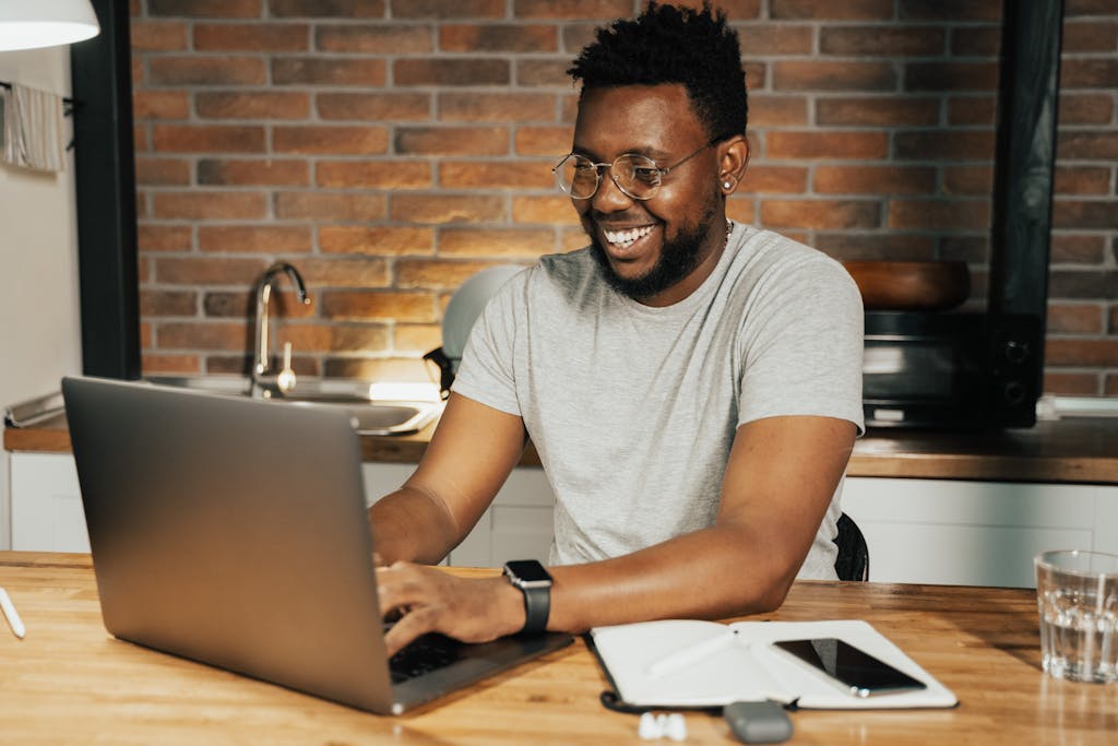 African American man smiling while working remotely on laptop from home office. He owns a sole proprietorship. 
