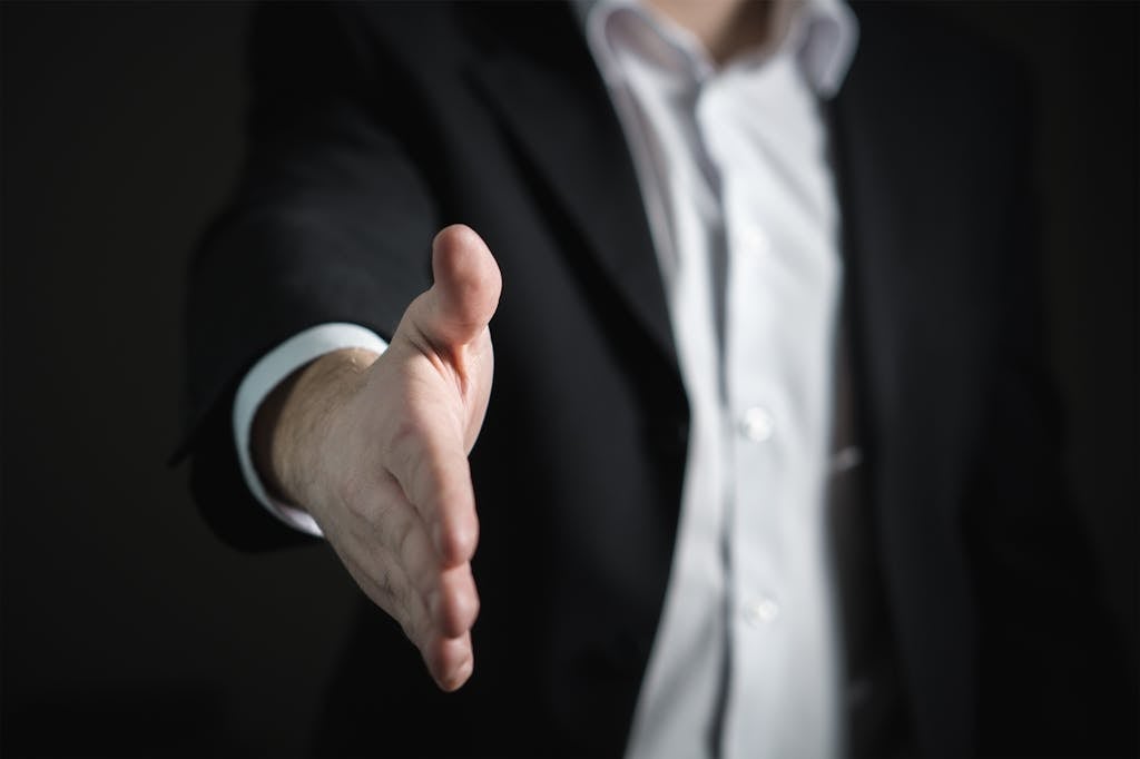 Close-up of a businessman extending hand for a handshake, symbolizing agreement and partnership to avoid breach of fiduciary duty.