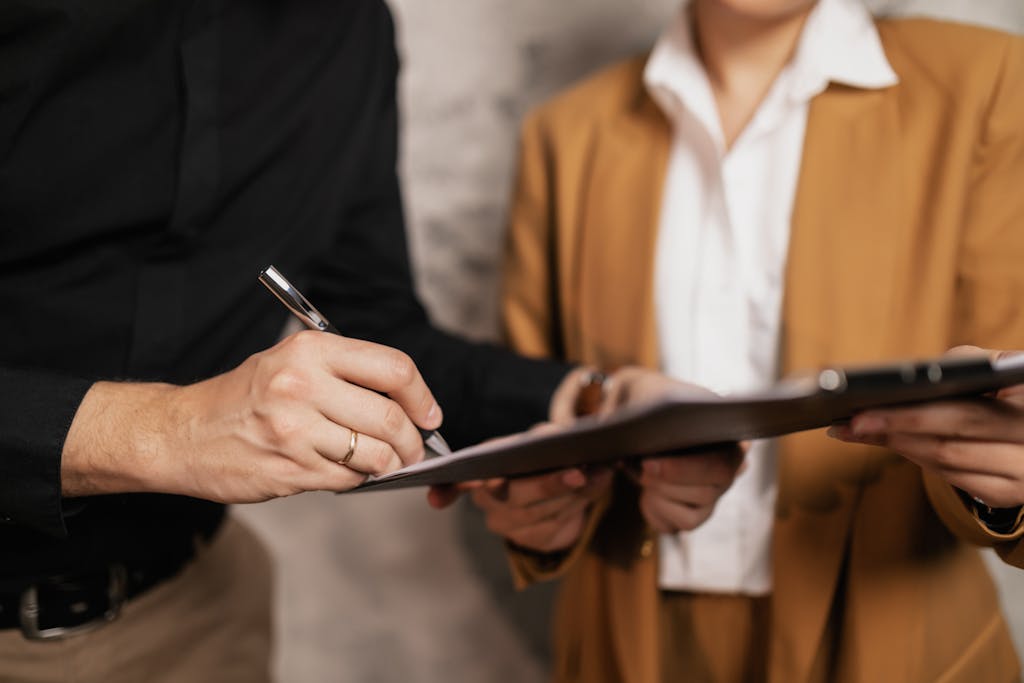 Close-up of two professionals signing a power of attorney paper work indoors, focus on hands and pen.