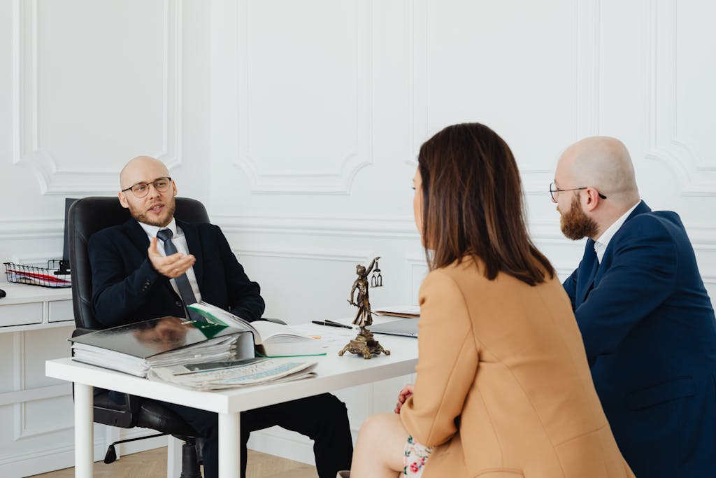 Three adults in a formal business meeting discussing legal matters of the differences between patent, copyright, and trademark in an office. 