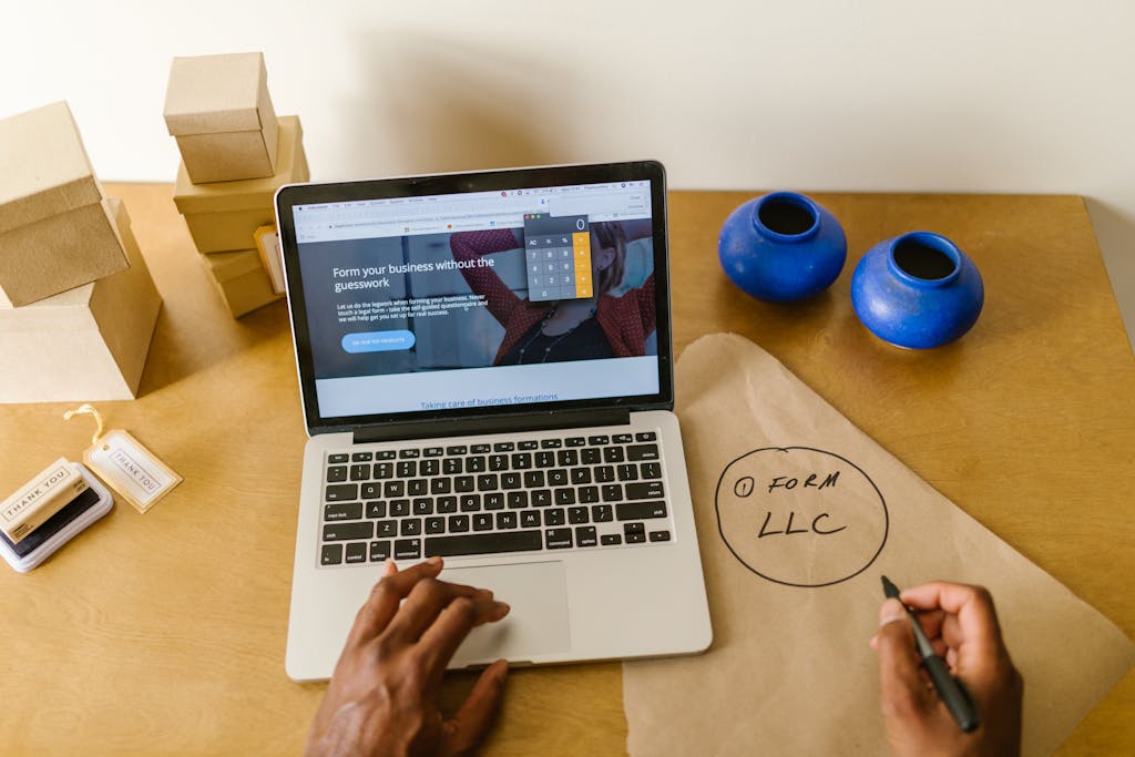 Workspace with laptop, packaging, and handwritten LLC notes, ideal for a small business startup scene researching how to obtain his EIN number. 
